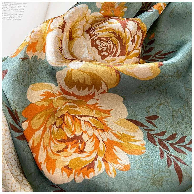 Close-up of golden-yellow blooming flowers and the smooth silky texture on a sage green satin scarf.
