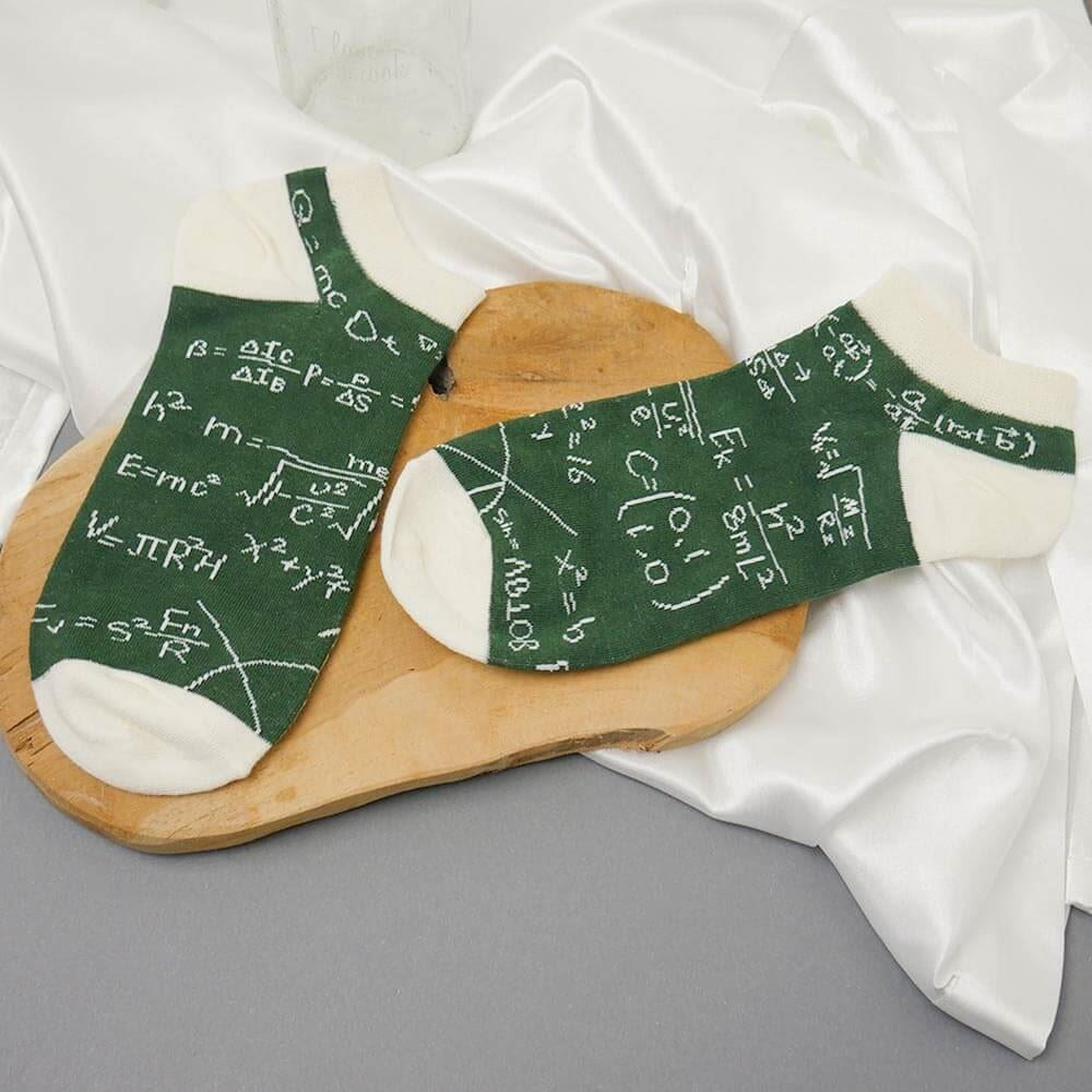 Green socks with mathematical equations on a wooden board and white fabric background