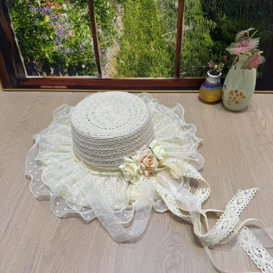 An ivory Victorian-style bonnet hat with a woven papyrus crown and a ruffled cotton lace brim, decorated with cream and pink roses and long trailing lace ribbons.