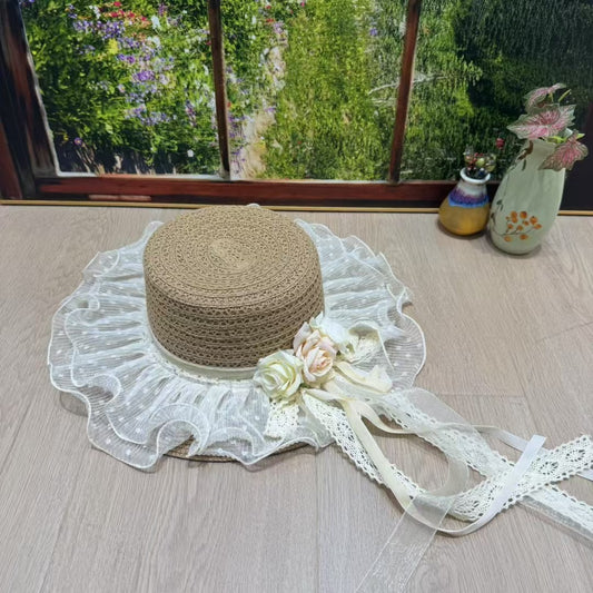 A Victorian-style bonnet hat with a brown woven papyrus crown and a wide, ruffled ivory cotton lace brim, decorated with cream and peach roses and long lace tie-ribbons.