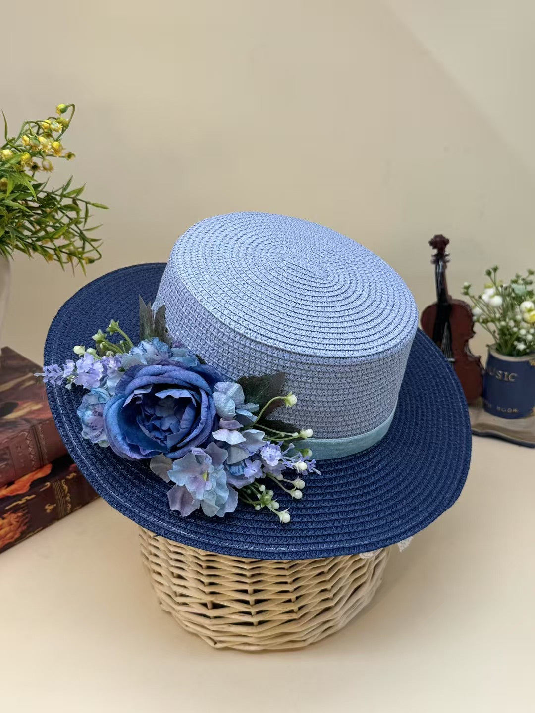 Vintage blue floral boater hat made of papyrus with layered blue flowers and ribbon, displayed on wicker basket with garden-themed decor.