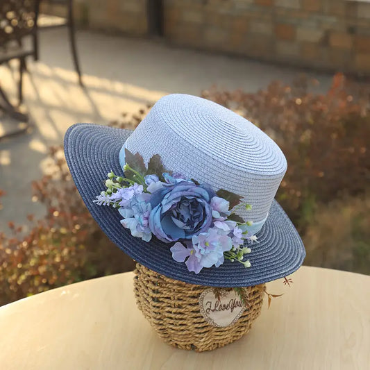 Vintage blue floral boater hat made of papyrus with layered blue flowers and ribbon, displayed on wicker basket with garden-themed decor.