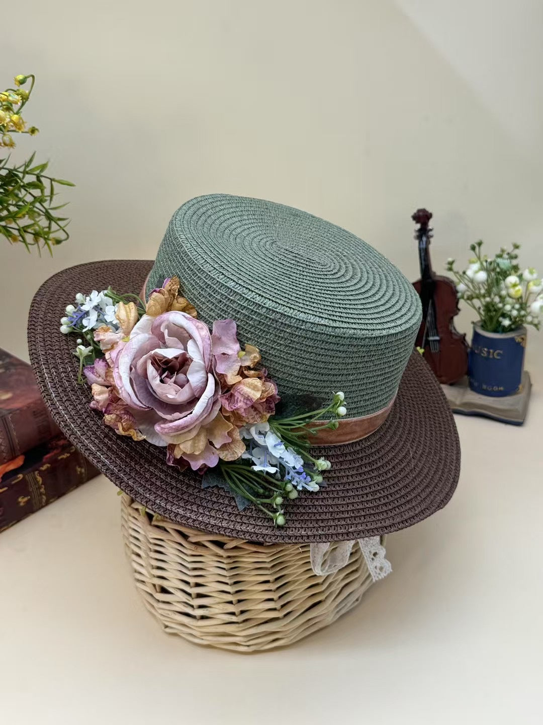 Vintage green and brown floral boater hat made of papyrus with soft mauve, blush, and cream flowers, styled on wicker basket with rustic decor.