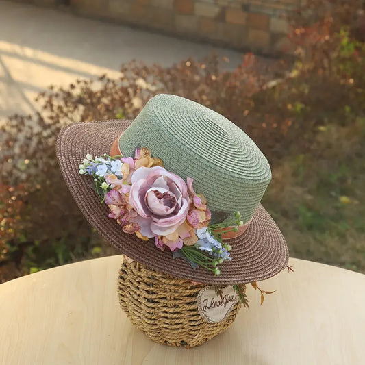 Vintage green and brown floral boater hat made of papyrus with soft mauve, blush, and cream flowers, styled on wicker basket with rustic decor.