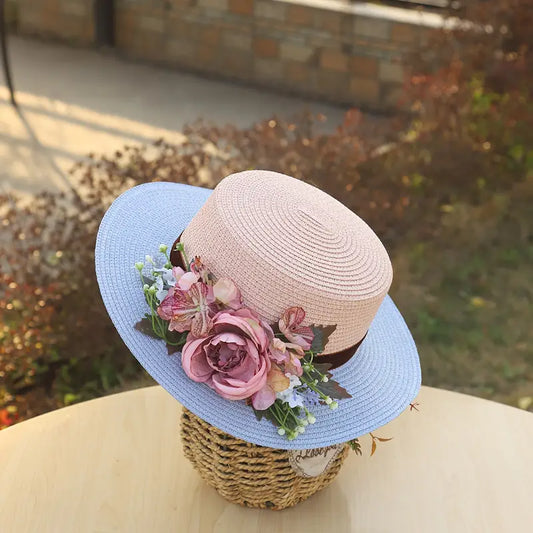 Vintage pink and blue floral boater hat made of papyrus with mauve roses and greenery, displayed on wicker basket with rustic decor.