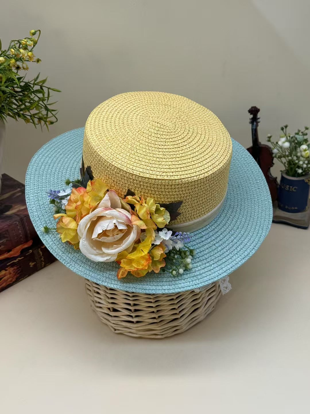 Vintage yellow and blue floral boater hat made of papyrus with yellow blossoms and cream rose, displayed on wicker basket with rustic decor.
