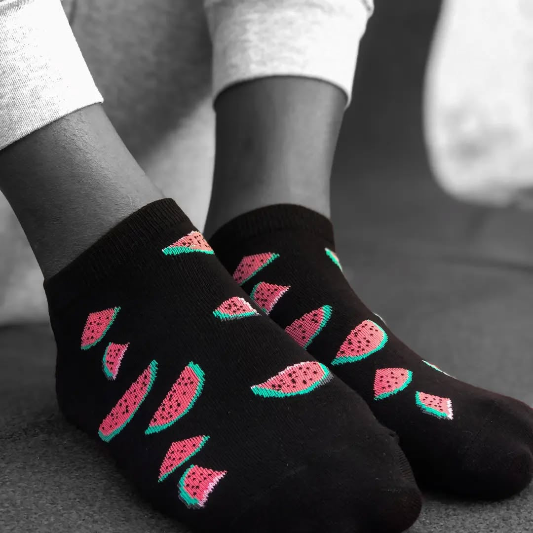 Black socks with watermelon pattern worn by a person on a neutral background