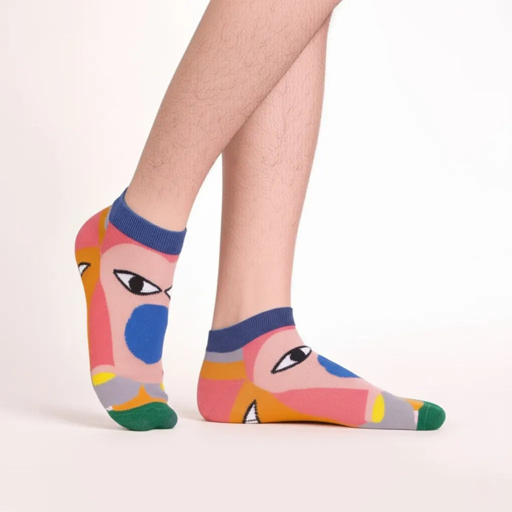Colorful socks with abstract face design worn by a person on a light pink background