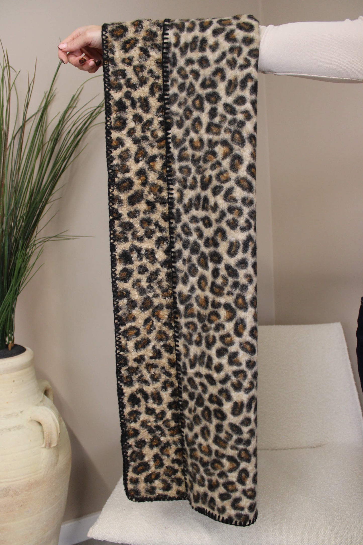 Leopard print brown scarf held by a person against a neutral background