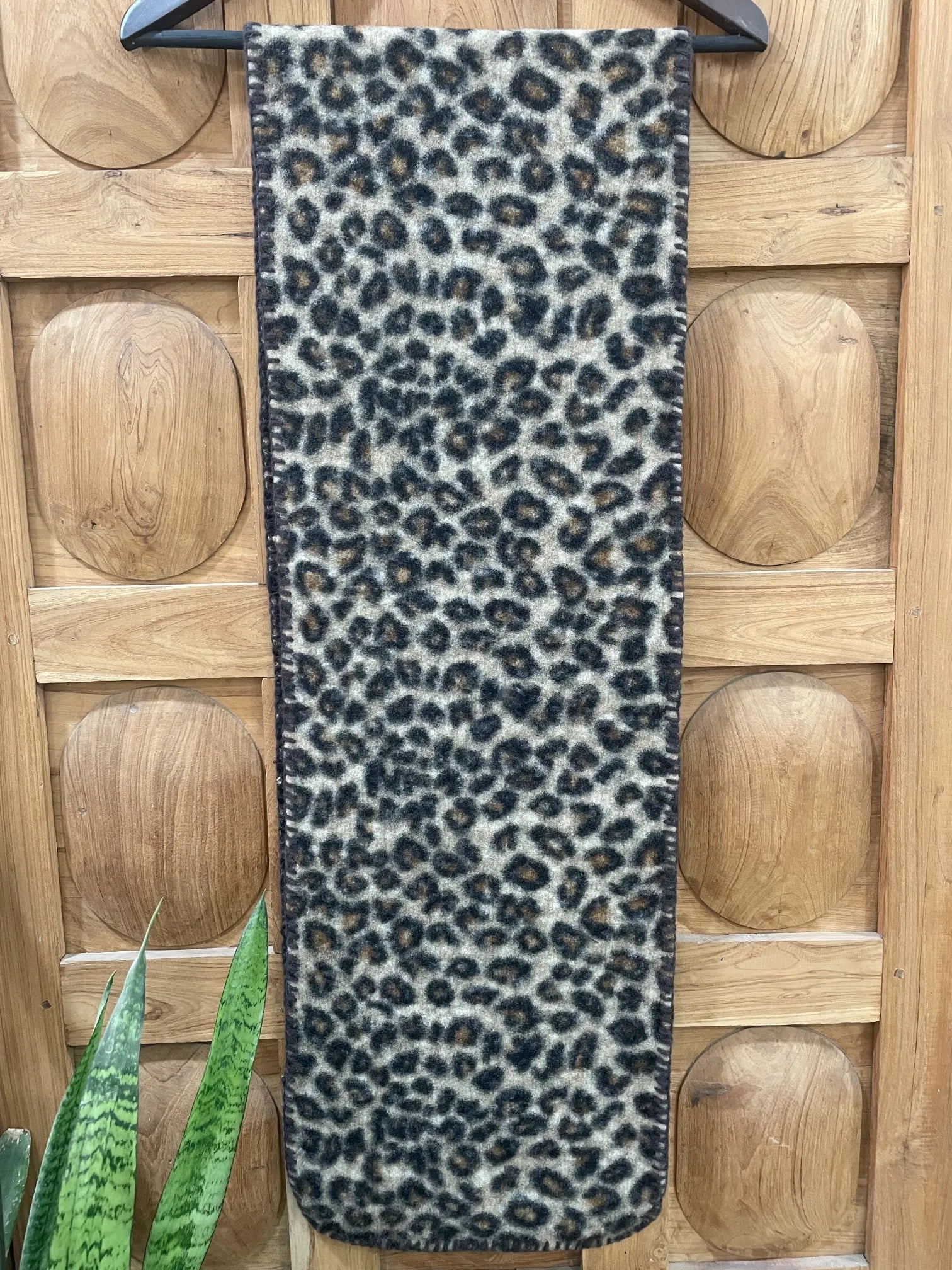 Leopard print scarf on a wooden floor with a plant in the corner