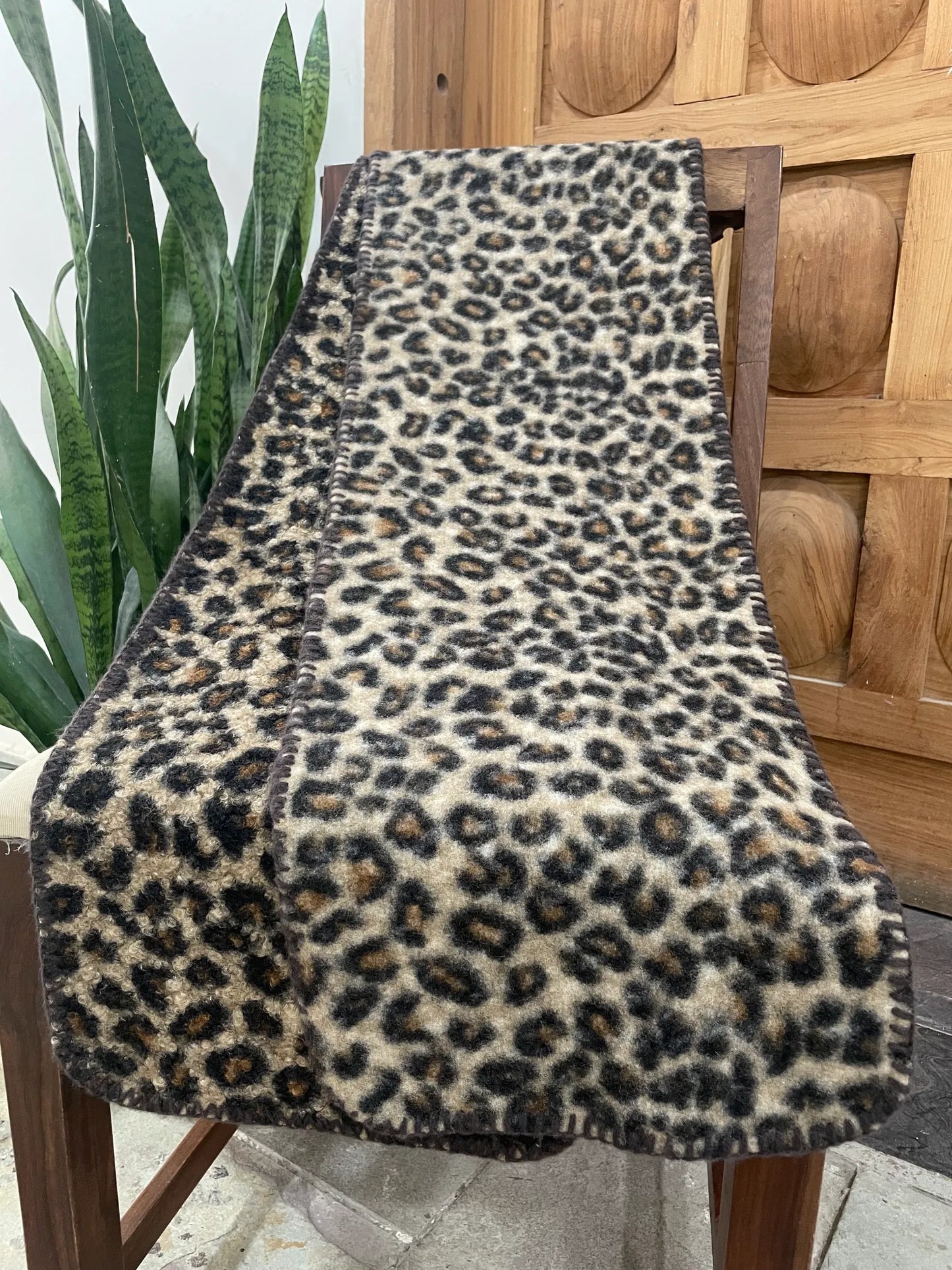 Leopard print scarf draped over a wooden chair with a plant in the background
