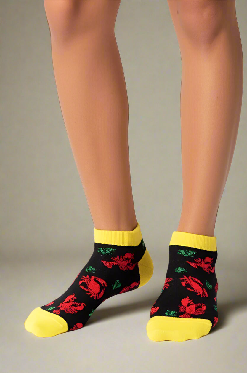 Black socks with colorful seafood designs, Lobsters and crabs,  and yellow toes and cuffs worn by a person on a white background