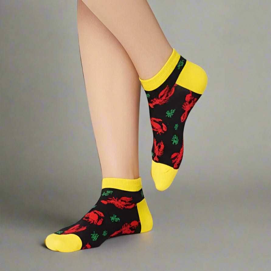 Person wearing black socks with red lobster design and yellow accents on a light gray background