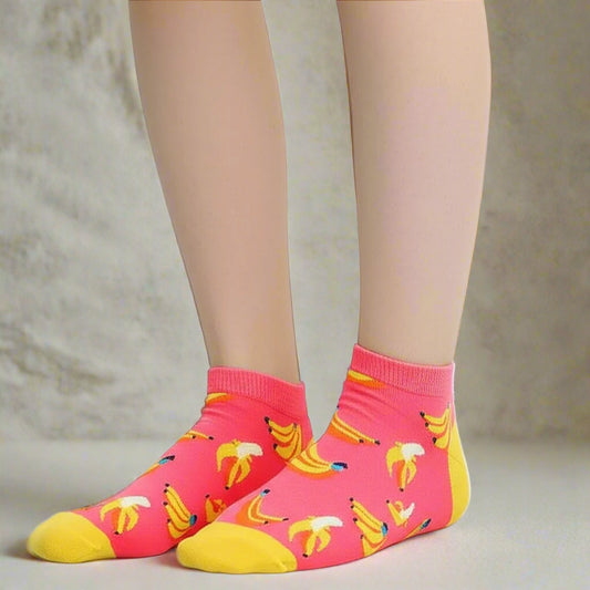Pink socks with cute banana pattern worn by a person on a light gray background