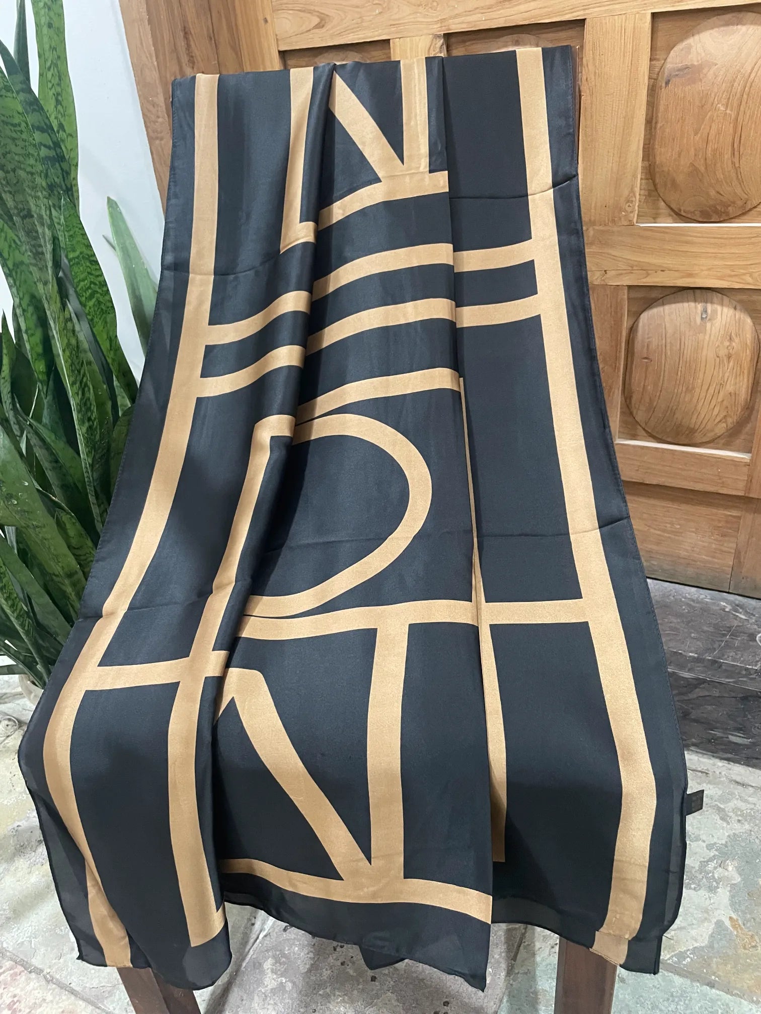 Full length view of the oversized geometric print on a black and gold satin scarf draped over a chair