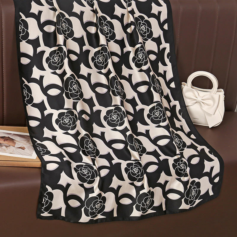 Discover timeless chic with this luxurious silk-feel satin scarf. Features a striking black and white design blending camellia flowers with a bold monogram pattern. Measures 90 x 180 cm. The perfect sophisticated accessory.