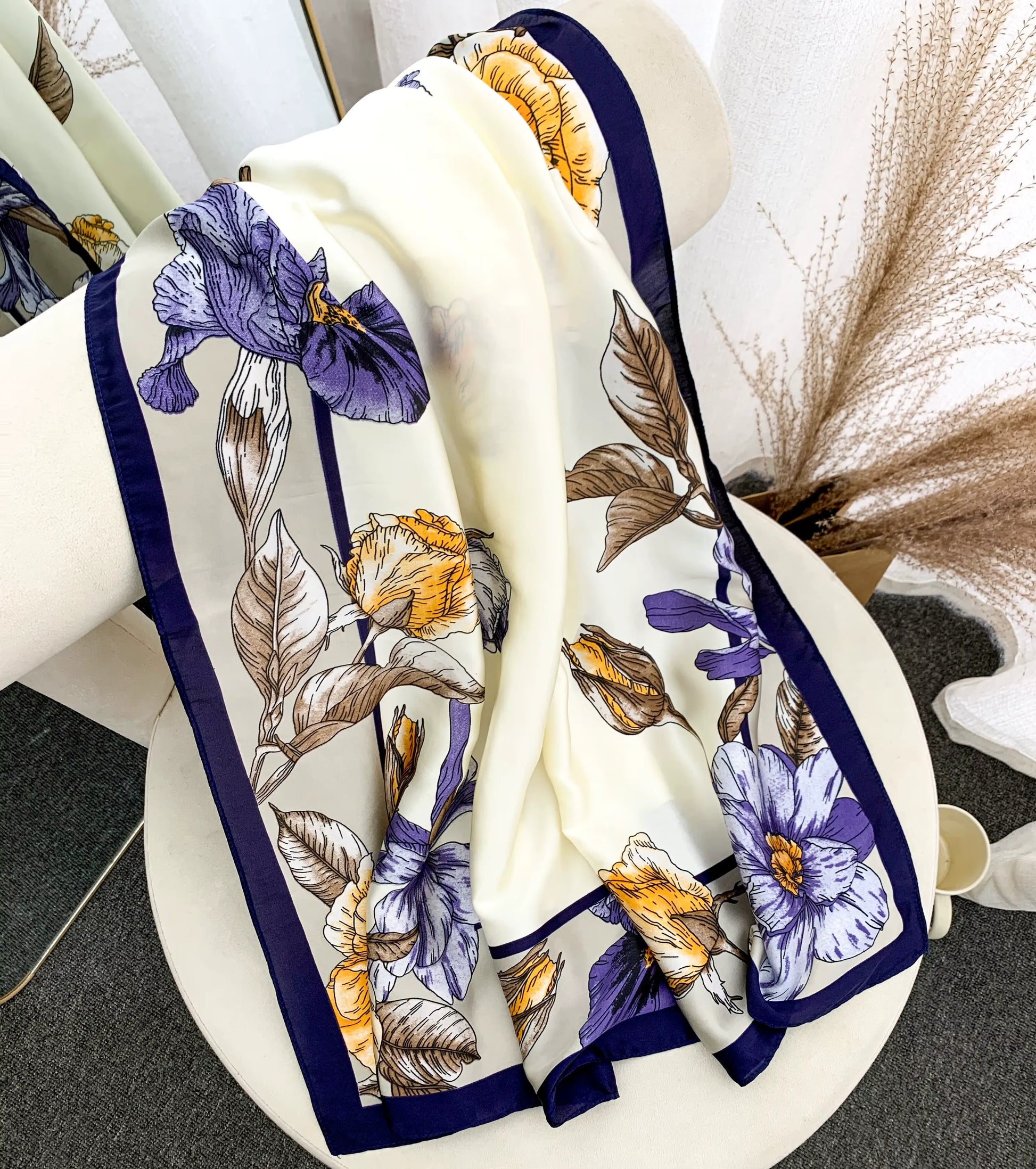 Close-up of a vintage-inspired floral satin scarf featuring irises and a deep navy border, tied elegantly on a chair. 