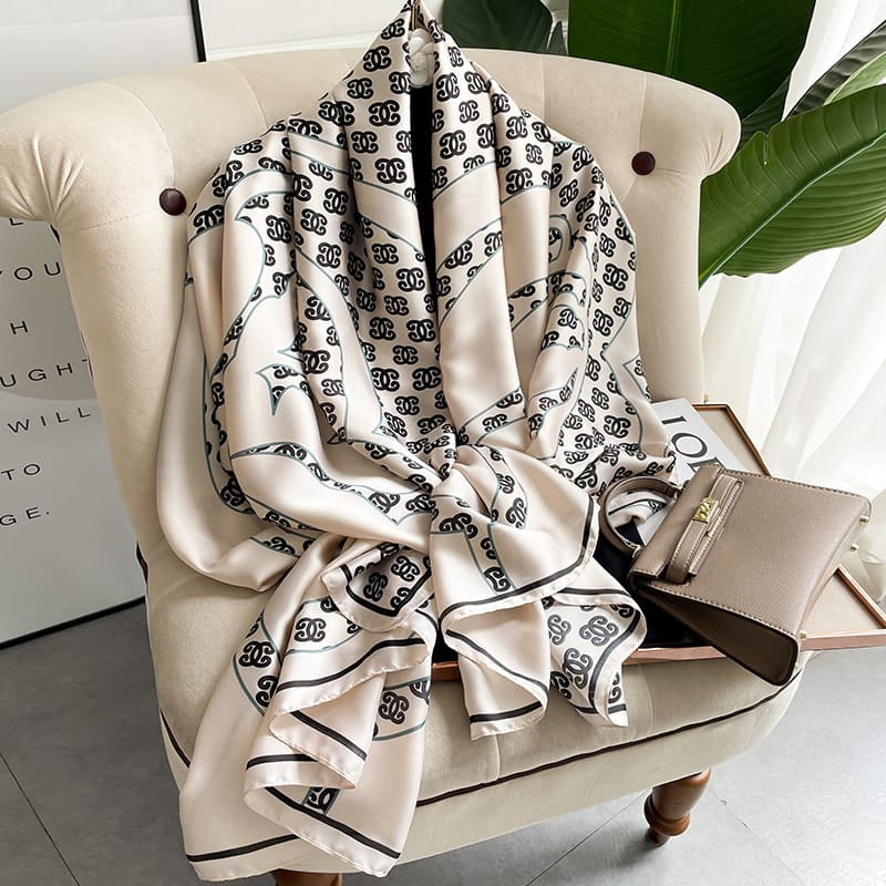 Experience timeless elegance with this luxurious silk-feel satin scarf. Features a chic cream and black monogram arranged in a sophisticated chain pattern. Measures 90 x 180 cm. The perfect accessory for any occasion.