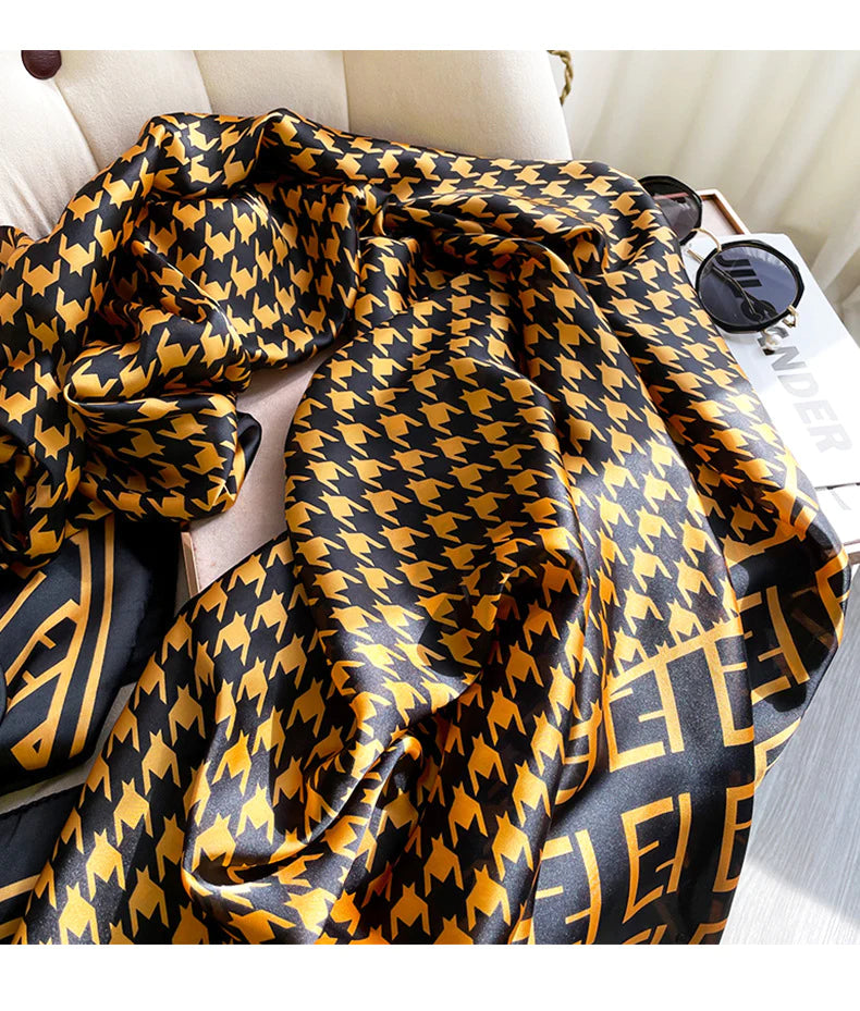 Elevate your wardrobe with this luxurious silk-feel satin scarf. Featuring a timeless gold and black houndstooth pattern complemented by a modern monogram border, this 90 x 180 cm scarf is the definition of chic.