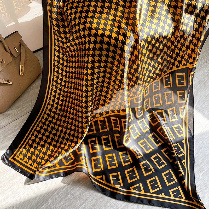 Elevate your wardrobe with this luxurious silk-feel satin scarf. Featuring a timeless gold and black houndstooth pattern complemented by a modern monogram border, this 90 x 180 cm scarf is the definition of chic.