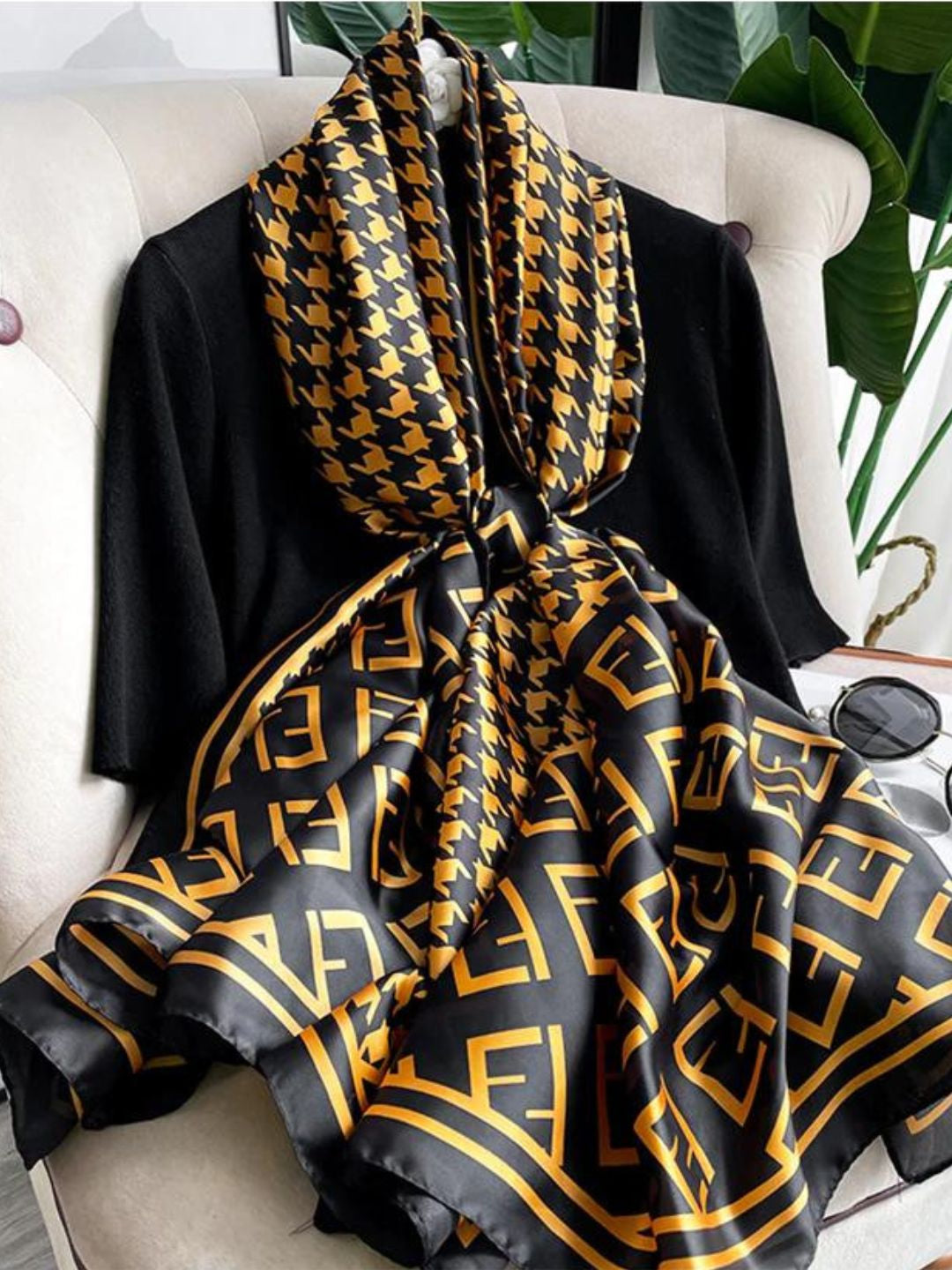 Elevate your wardrobe with this luxurious silk-feel satin scarf. Featuring a timeless gold and black houndstooth pattern complemented by a modern monogram border, this 90 x 180 cm scarf is the definition of chic. 