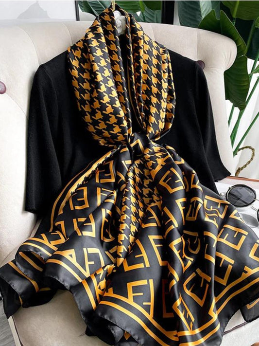 Elevate your wardrobe with this luxurious silk-feel satin scarf. Featuring a timeless gold and black houndstooth pattern complemented by a modern monogram border, this 90 x 180 cm scarf is the definition of chic. 